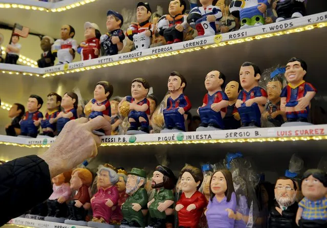 A vendor takes a clay "caganer" resprenting Lionel Messi from the stands at the Santa Llucia Christmas market in central Barcelona, Spain, December 16, 2015. (Photo by Albert Gea/Reuters)