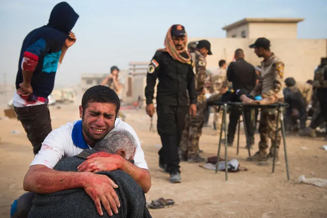 Father and grandfather of 15-year-old Shafiq mourn as Iraqi forces surround his body at an outdoor field clinic in the Samah neighbourhood in Mosul on November 13, 2016. A double barreled mortar attack killed Shafiq and seriously injured his 12-year-old neighbour Mohammed as Iraqi Special Forces 2nd division continued to battle IS forces as they pushed through the Arbagiah area and into the neigbourhood of Karkukli. (Photo by Odd Andersen/AFP Photo)