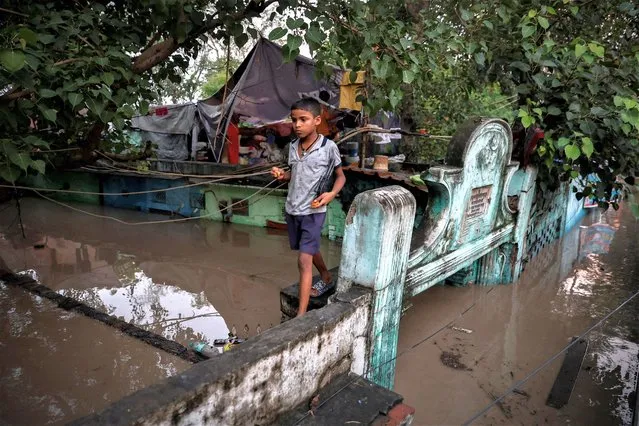 A boy walks on a wall of his flooded house after a rise in the water level of river Yamuna in New Delhi, India on July 12, 2023. (Photo by Adnan Abidi/Reuters)