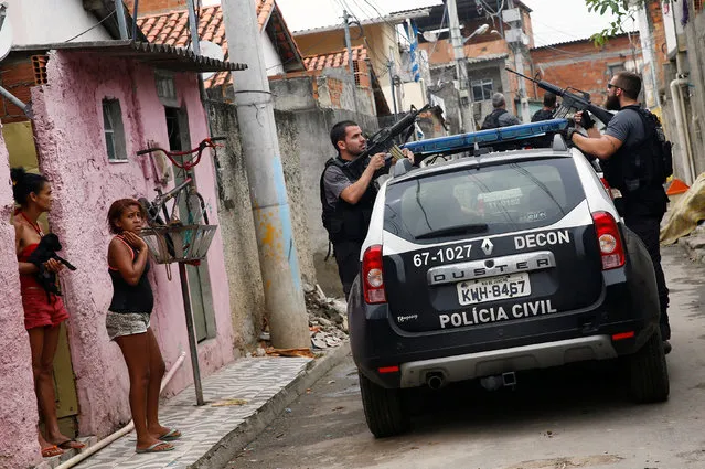 Policemen take position near residents during an operation against drug dealers in Cidade de Deus or City of God slum in Rio de Janeiro, Brazil, November 23, 2016. (Photo by Ricardo Moraes/Reuters)