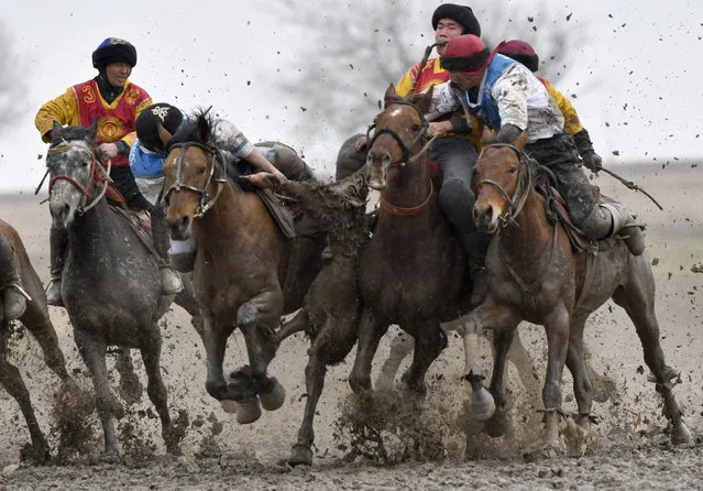 Riders compete during a kok boru, also called ulak tartysh, a traditional game in which players on horseback manoeuvre with a goat's carcass and score by putting it into the opponents' goal outside Sokuluk village, 20 km (12,5 miles) west of Bishkek, Kyrgyzstan, Tuesday, March 30, 2021. (Photo by Vladimir Voronin/AP Photo)