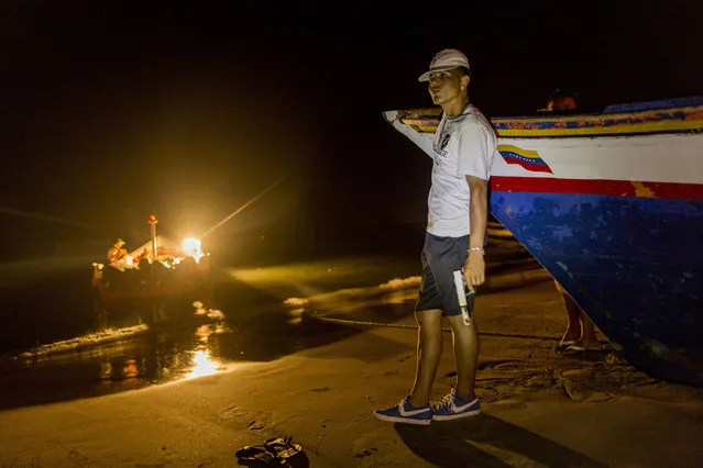 In this November 2, 2016 photo, a member of the Marval fishing family who goes by the nickname “El Chukiti” holds a homemade gun as he guards against a possible pirate attack as fishermen unload their catch in Punta de Araya, Sucre state, Venezuela. The family's self-defense group calls themselves “Los Cainos”. (Photo by Rodrigo Abd/AP Photo)