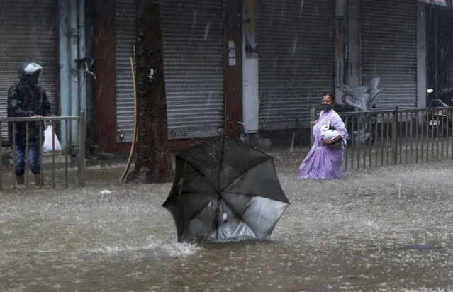 A woman helplessly watches her umbrella fly away in the wind during a heavy rain in Mumbai, India, Monday, May 17, 2021. Cyclone Tauktae, roaring in the Arabian Sea was moving toward India's western coast on Monday as authorities tried to evacuate hundreds of thousands of people and suspended COVID-19 vaccinations in one state. (Photo by Rajanish Kakade/AP Photo)