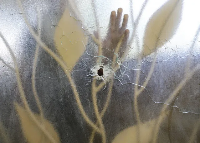 A hospital worker places his hand on a glass door within the clinic that was pierced by a bullet the previous day during an attack on the Fontaine Hospital Center in the Cité Soleil area of Port-au-Prince, Haiti, Thursday, November 16, 2023. A heavily armed gang surrounded the hospital on Wednesday, trapping women, children and newborns inside until police rescued them, according to the director of the medical center. (Photo by Odelyn Joseph/AP Photo)