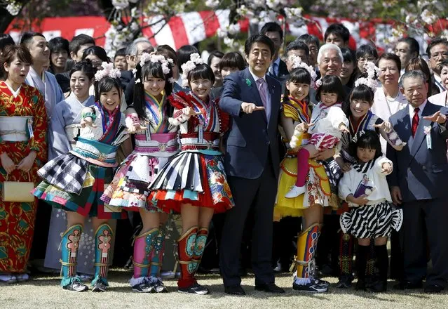 Japan's Prime Minister Shinzo Abe (C) poses with members of Japanese idol group Momoiro Clover Z and other show-business celebrities at a cherry blossom viewing party at Shinjuku Gyoen park in Tokyo April 18, 2015. Thousands of people including entertainers, athletes and politicians were invited to the annual party hosted by Abe. (Photo by Issei Kato/Reuters)