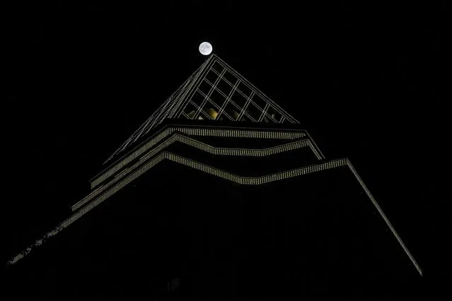 The full moon rises over a building during the Mid-autumn festival also known as mooncake festival in Beijing, China, Tuesday, September 21, 2021. (Photo by Ng Han Guan/AP Photo)