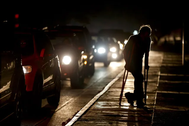 In this March 29, 2019 file photo, a man on crutches is illuminated by headlights of oncoming traffic, in Caracas, Venezuela. Venezuelans are struggling to understand the Sunday, March 31, 2019 announcement that the nation’s electricity is being rationed to combat daily blackouts. (Photo by Natacha Pisarenko/AP Photo)