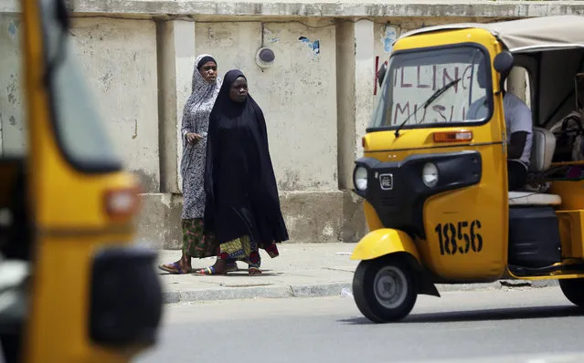 Muslim women walk past tricycle taxis partially hiding a sign reading “Stop killing Muslims Army” on the walls in Kano , Nigeria, Friday, April. 8, 2016. A human rights lawyer says the detained leader of Nigeria's Shiite Muslims has been left near-blind and suffered several operations to remove bullets from gunshots in an army raid on his home. (Photo by Sunday Alamba/AP Photo)