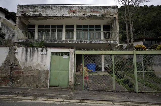 Architect Rudiar Almeida, 76, closes the gate to his home in Caracas, Venezuela, Friday, December 10, 2021. Almeida says that his monthly pension is equal to two U.S. dollars and it is not enough to buy food. He lives alone in what was his parents' home but does not have the money to maintain it. His only son emigrated to Colombia two years ago and has not heard from him since. (Photo by Ariana Cubillos/AP Photo)