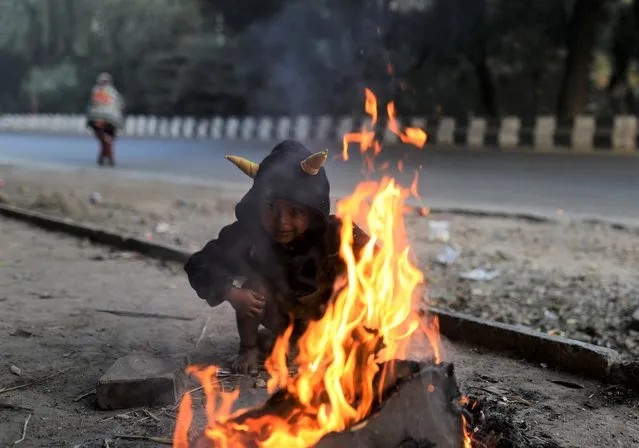 A child sits next to a campfire on a cold winter morning in New Delhi, India, December 17, 2021. (Photo by Anushree Fadnavis/Reuters)
