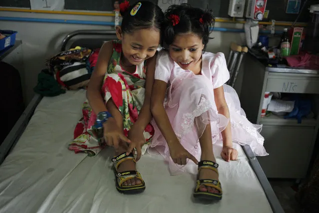 In this July 15, 2015 photo, Nepalese amputee victims Khendo Tamang, left, and Nirmala Pariyar, both 8, share a single pair of shoes at the Bir Trauma Center in Kathmandu, Nepal. After suffering serious leg wounds in Nepal's massive 2015 earthquake that killed and injured thousands, both girls were brought to the Bir Trauma Center in Kathmandu, to receive single leg amputations. Following their surgeries, Nirmala's relentless cheerfulness drew a still very depressed Khendo close and both found an inseparable friendship which has helped their emotional wounds heal. (Photo by Niranjan Shrestha/AP Photo)