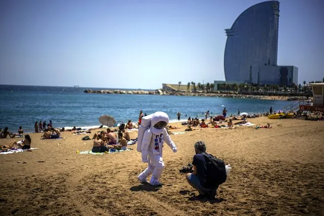 A man films a person dressed as an astronaut on the beach of Barcelona, Spain, Friday, July 9, 2021. Spain's top diplomat is pushing back against French cautions over vacationing on the Iberian peninsula. Southern Europe's holiday hotspots worry that repeated changes to rules on who can visit is putting people off travel. On Thursday, France's secretary of state for European affairs, Clement Beaune, advised people to “avoid Spain and Portugal as destinations” when booking their holidays because COVID-19 infections are surging there. (Photo by Joan Mateu/AP Photo)
