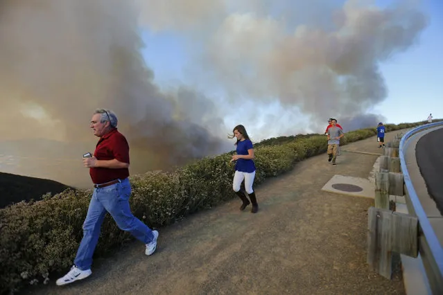 After climbing a hillside to view the so-called Poinsettia Fire, residents are evacuated by police as yet another wildfire near San Diego moves up a hillside near San Marcos, California May 14, 2014. At least two structures burned to the ground and some 15,000 homes and businesses were told to evacuate on Wednesday as the wind-lashed Poinsettia wildfire roared out of control in the heart of a Southern California coastal community. (Photo by Mike Blake/Reuters)