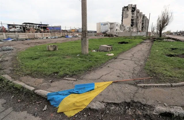 A Ukrainian state flag is seen on the pavement near buildings damaged during Ukraine-Russia conflict in the southern port city of Mariupol, Ukraine on April 22, 2022. (Photo by Alexander Ermochenko/Reuters)