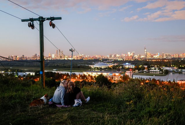 Two women and a dog rest on a hill with the view on city's skyline during sunset time in Moscow, Russia on July 23, 2024. (Photo by Maxim Shemetov/Reuters)