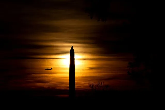 A plane flies past the Washington Monument at sunset in Washington, DC, on March 14, 2022. (Photo by Stefani Reynolds/AFP Photo)
