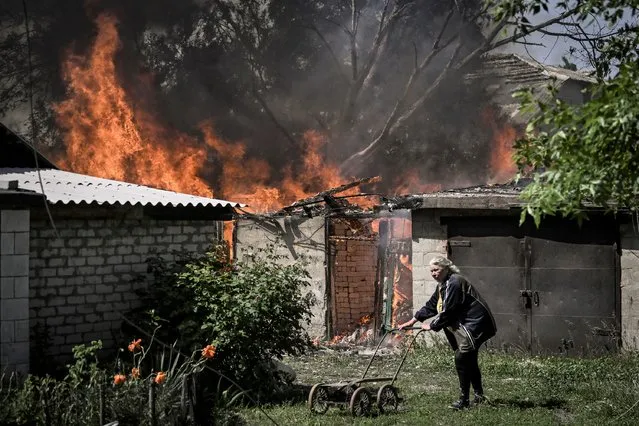 An elderly woman walks away from a burning house garage after shelling in the city of Lysytsansk at the eastern Ukrainian region of Donbas on May 30, 2022, on the 96th day of the Russian invasion of Ukraine. Since failing to capture Kyiv in the war's early stages, Russia's army has narrowed its focus, hammering Donbas cities with artillery and missile barrages as it seeks to consolidate its control. (Photo by Aris Messinis/AFP Photo)