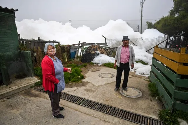 A man and a woman stand near pungent foam which formed in the polluted Mosquera River and invaded the Los Puentes neighbourhood, west of Bogota, on April 26, 2022. (Photo by Juan Barreto/AFP Photo)