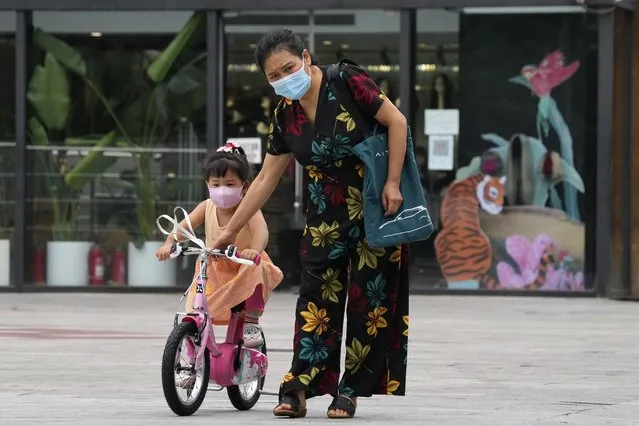A woman helps a child with her bike on the street, Wednesday, July 6, 2022, in Beijing. (Photo by Ng Han Guan/AP Photo)