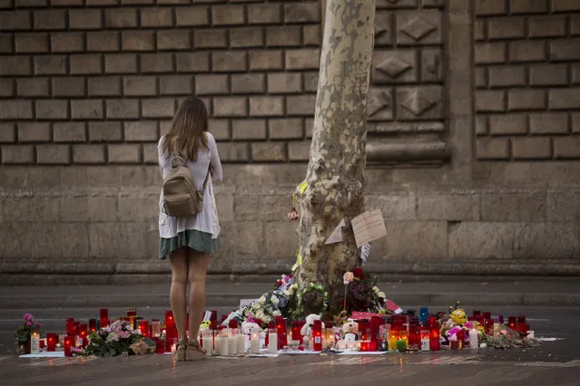 A woman stands next to candles and flowers after a van attack that killed at least 14 people in Las Ramblas promenade, Spain, Monday, August 21, 2017. (Photo by Emilio Morenatt/AP Photoi)