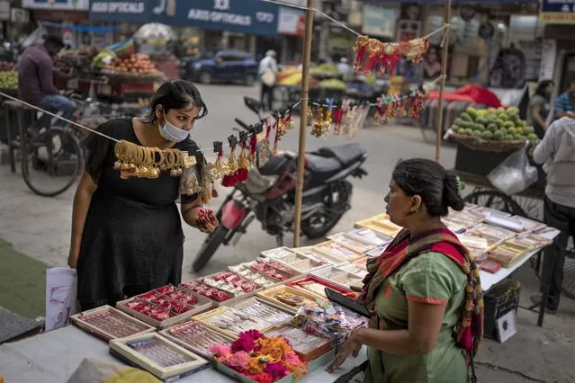 A woman wearing masks as a precaution against coronavirus shops for artificial jewelry from a roadside vendor in New Delhi, India, Thursday, August 11, 2022. (Photo by Altaf Qadri/AP Photo)