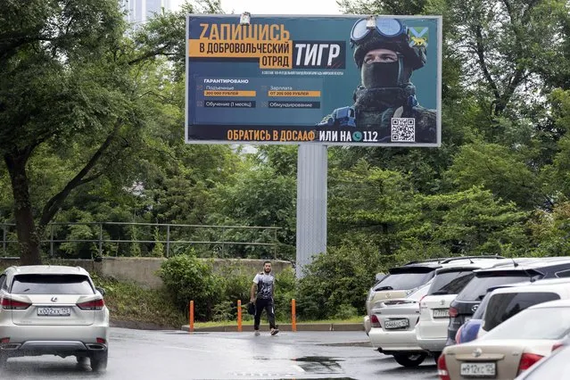 A person walks past a billboard reading “Sign up for a volunteer team” encouraging Russians to sign up for the Tiger volunteer battalion, at the far-eastern Primorye region in a street of Vladivostok, Russia, Thursday, August 11, 2022. Colorful billboards and ads on public transport in different Russian regions state that "heroes are wanted" and urge Russian men to join the professional army ranks. (Photo by AP Photo/Stringer)