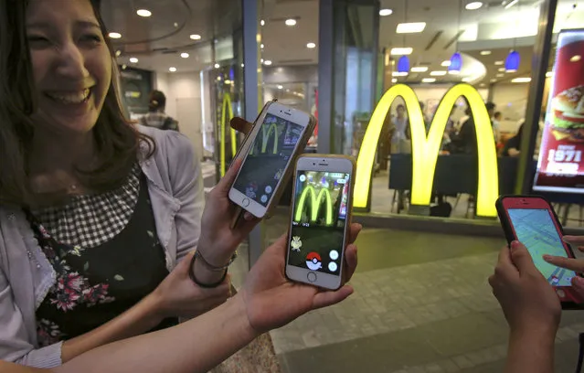 Women play “Pokemon Go” in front of a McDonald's restaurant in Tokyo, Friday, July 22, 2016.  The Japan launch of “Pokemon Go” on Friday included the game's first partnership with an outside company: fast-food giant McDonald's. About 400 McDonald's Japan outlets are “gyms”, where players can battle on their smartphones. The other 2,500 are “Pokestops”, where they can get items to play the game. The hope is, presumably, that they may also buy a Big Mac in the process. (Photo by Koji Sasahara/AP Photo)