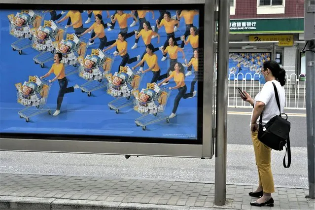 A resident waits at a bus-stop near an ad depicting shoppers in Beijing, Saturday, August 15, 2022. (Photo by Ng Han Guan/AP Photo)