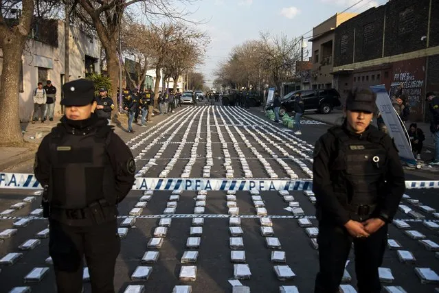 Police stand guard over seized packages of cocaine displayed to the press in Rosario, Santa Fe province, Argentina on August 26, 2022. Federal Police officers seized more than 1,600 kilos of cocaine, valued at some US$60 million, which were about to leave through the waterway to Dubai, authorities said. (Photo by AFP Photo/Stringer)