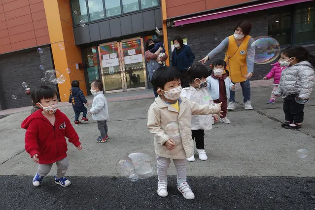 Children wearing face masks to help protect against the spread of the new coronavirus watch soap bubbles fly at the Chogyesa temple in South Korea, Friday, April 24, 2020. (Photo by Ahn Young-joon/AP Photo)