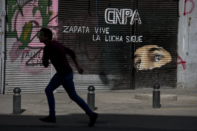 A boy playing soccer in a street outside the Interior Ministry that was barricaded by police runs past a mural of rebel leader Sub Comandante Marcos with the slogan in Spanish “Zapata lives. The struggle continues”, in Mexico City, Wednesday, June 22, 2016. A group of protesting teachers accompanied by a mediation commission were meeting Wednesday evening with Interior Secretary Miguel Angel Osorio Chong. The negotiations between the striking radical teachers and the government come three days after a clash between protestors and police in Oaxaca state left eight dead and more than 100 injured. (Photo by Rebecca Blackwell/AP Photo)