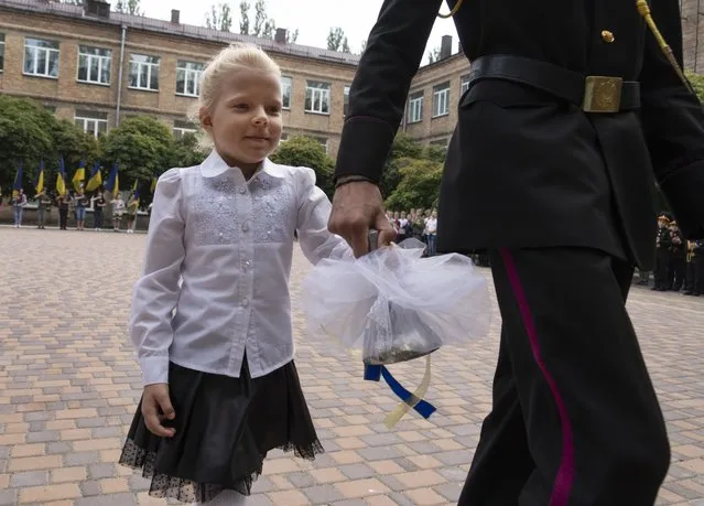 A graduate cadet holds the hand of a young schoolgirl and rings the bell on the first day of school at a cadet lyceum in Kyiv, Ukraine, Thursday, September 1, 2022. (Photo by Efrem Lukatsky/AP Photo)