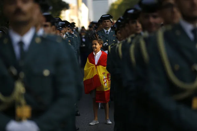 A young boy, draped in the Spanish flag, stand amongst Spanish military personnel as they prepare for a military parade during the national holiday known as “Dia de la Hispanidad” or Hispanic Day, in Madrid, Spain, Thursday, October 12, 2017. King Felipe VI is to preside over the annual colorful parade Thursday as Spain awaits a response to a government request to Catalonia to clarify by Monday if it has already declared independence, in which case Spain warns it may begin taking control of the region. (Photo by Francisco Seco/AP Photo)