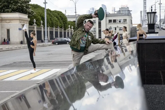 A Russian Border Guard veteran tries to to stretch in front of members of stretching class record their excises as he comes to celebrate Border Guards service holiday at closed due to coronavirus pandemic Gorky Park in Moscow, Russia, Thursday, May 28, 2020. Russia marked the 102nd anniversary of its Border Guards on Thursday. (Photo by Alexander Zemlianichenko/AP Photo)