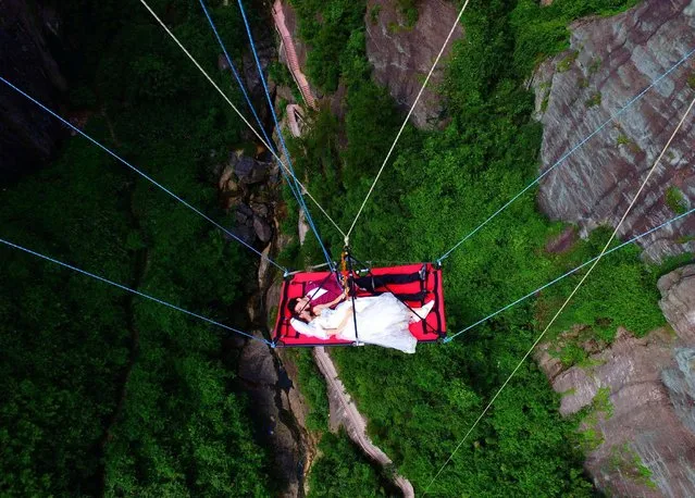 A newly married couple lie on a canvas mat as they are lowered from a glass bridge during a promotional event for the tourist spot, on Chinese Valentines' Day in Pingjiang, Hunan province, China, August 9, 2016. (Photo by Reuters/China Daily)
