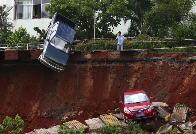 A man looks on as cars are seen stuck in a sinkhole that occurred in a parking area after heavy rainfall hit Haikou, Hainan province, China, September 16, 2015. No casualty has been reported. (Photo by Reuters/Stringer)