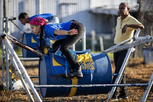 Jockey student Mariangelys Almedina (Front) balances on a steel drum suspended in the air by a series of springs to simulate riding a horse as Instructor Willie Lozano looks on at the Vocational Equestrian Agustín Mercado Reverón School located in the Hipódromo Camarero on November 17, 2022 in Canovanas, Puerto Rico. The Vocational Equestrian Agustín Mercado Reverón School has produced some of the best jockeys in the world but also prepares students for a wide range of equestrian jobs on a tuition-free basis. (Photo by Al Bello/Getty Images)