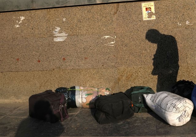 The shadow of a migrant worker from another state is cast over his belongings as he waits for transportation, Monday, November 21, 2022,  in New Delhi. (Photo by Manish Swarup/AP Photo)