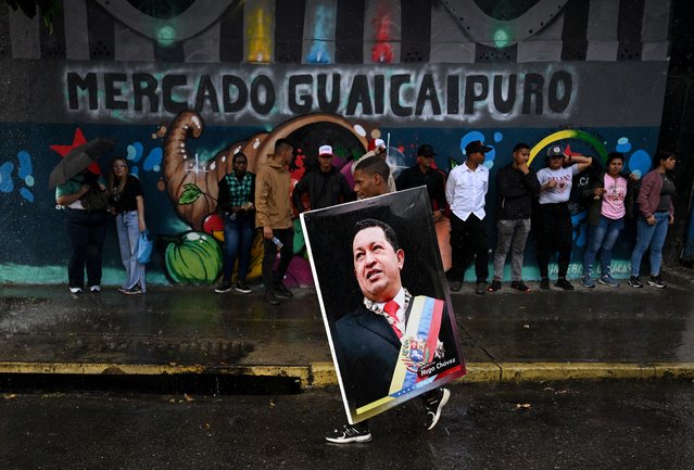 A supporter of Venezuela's President Nicolas Maduro holds an image of late Venezuela's President Hugo Chavez during a rally to celebrate the first anniversary of his re-election in Caracas on July 28, 2025. (Photo by Federico Parra/AFP Photo)