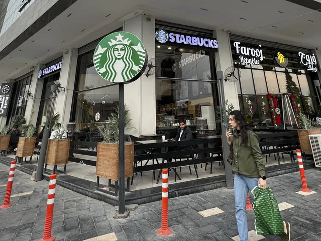 A woman walks by an unlicensed Starbucks cafe in Baghdad, Iraq, Wednesday, December 21, 2022. Real Starbucks merchandise is imported from neighboring countries to stock the three cafes in the city, but all are unlicensed. Starbucks filed a lawsuit in an attempt to shut down the trademark violation but the case was shuttered after the owner allegedly threatened lawyers hired by the coffee house. (Photo by Ali Abdul Hassan/AP Photo)