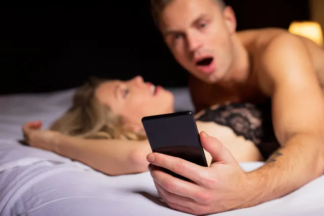 Surprised man looking at his phone while laying on top of woman. (Photo by Getty Images/iStockphoto)