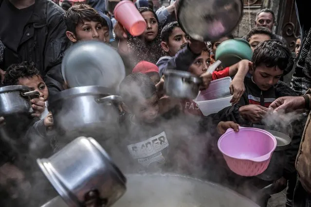 Youths hold out their pots and containers to receive soup prepared by Palestinian Walid al-Hattab (not pictured) as they break their fast on the second day of the Muslim holy month of Ramadan in Gaza City on March 24, 2023. (Photo by Mohammed Abed/AFP Photo)