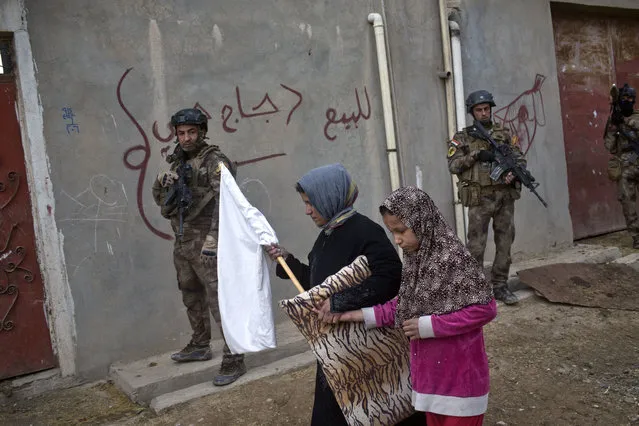 Civilians carry a white flag as they pass by Iraqi special forces on patrol in Gogjali, an eastern district of Mosul, Iraq, Wednesday, November 2, 2016. Iraqi special forces paused their advance in an eastern district of Mosul on Wednesday to clear a neighborhood of any remaining Islamic State militants, killing at least eight while carrying out house-to-house searches. (Photo by Marko Drobnjakovic/AP Photo)