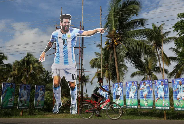 A boy rides his bicycle past a giant cut out of Argentina's soccer player Lionel Messi at a roadside, ahead of FIFA World Cup 2018 Group D match between Argentina and Iceland, on the outskirts of Kochi, India, June 15, 2018. (Photo by Sivaram V/Reuters)