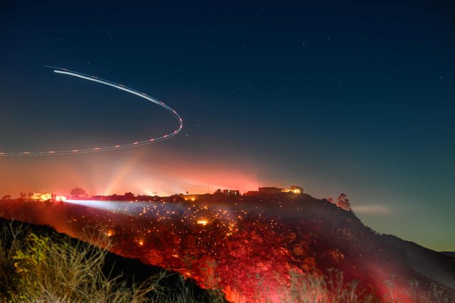 In this long exposure photo, a helicopter surveys the scene during the Lilac fire in unincorporated San Diego County, California on January 21, 2025. Exhausted Los Angeles firefighters on January 20 braced for the return of yet more dangerously strong gusts, as California's governor slammed “hurricane-force winds of misinformation” surrounding blazes that have killed 27 people. The two largest fires, which have obliterated almost 40,000 acres (16,000 hectares) and razed entire neighborhoods of the second biggest US city, were both now more than half contained, officials announced. (Photo by Josh Edelson/AFP Photo)