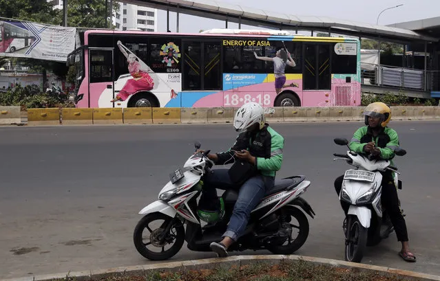 In this July 26, 2018, photo, motorcycle taxi drivers wait for customers as a bus with Asian Games promotional stickers drive past by at the main business district in Jakarta, Indonesia. (Photo by Tatan Syuflana/AP Photo)