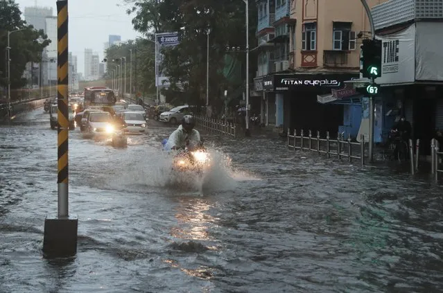 Commuters wade through a waterlogged street during a heavy rain in Mumbai, India, Monday, May 17, 2021. (Photo by Rajanish Kakade/AP Photo)