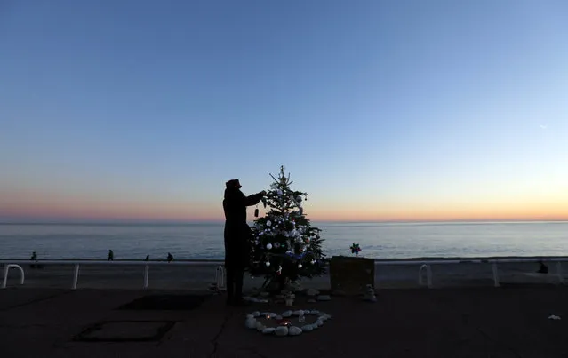 A passer-by adds a decoration to a Christmas tree placed in tribute to the victims of the summer truck attack on the Promenade Des Anglais in Nice, December 23, 2016. (Photo by Eric Gaillard/Reuters)