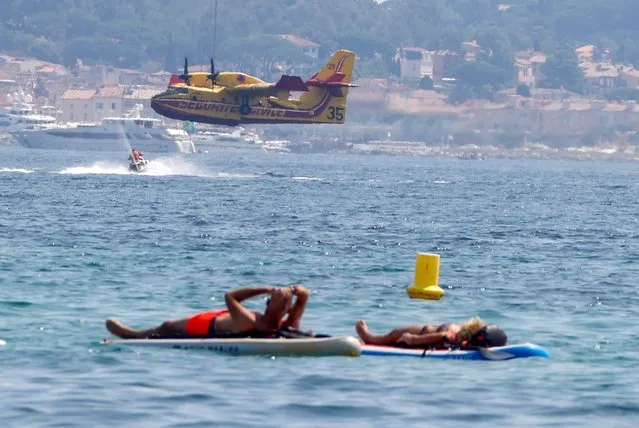 People float on boards as a Canadair aircraft flies after being filled up with water to help with efforts in extinguishing a major fire that broke out in the Var region, at the Gulf of Saint Tropez, France on August 17, 2021. (Photo by Eric Gaillard/Reuters)