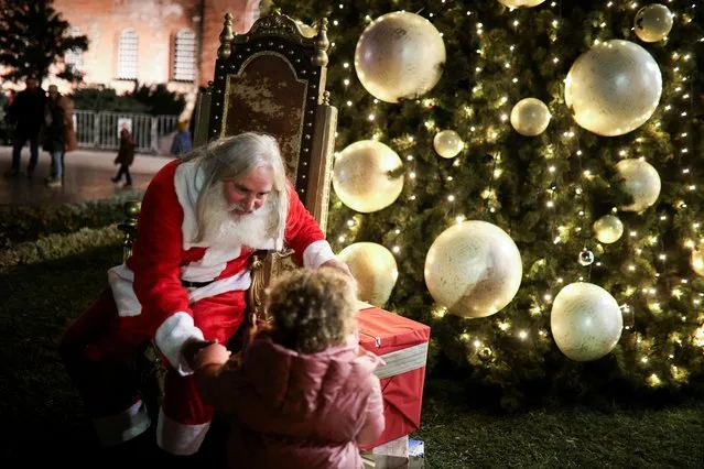 A man dressed in Santa Claus costume talks to a child in front of a Christmas tree during its lighting ceremony in front of the Alexander Nevsky cathedral in Sofia, Bulgaria on December 1, 2023. (Photo by Spasiyana Sergieva/Reuters)
